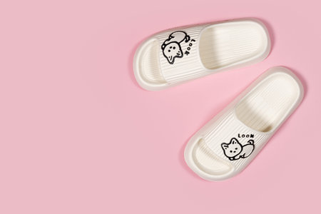 A pair of beige rubber slippers with cat on a pink background.