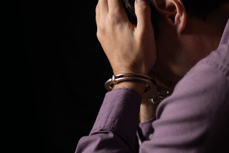 Businessman in handcuffs arrested for financial fraud, sitting in interrogation room.