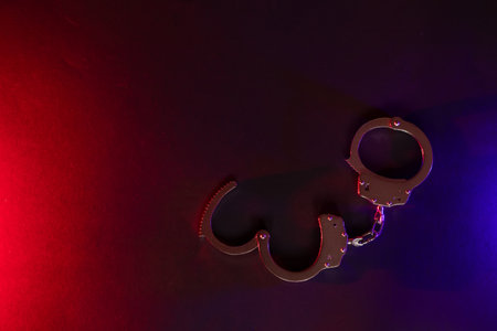 Police raid at night and you are under arrest concept. Silhouette of handcuffs. Image with the flashing red and blue police lights dark background.の写真素材