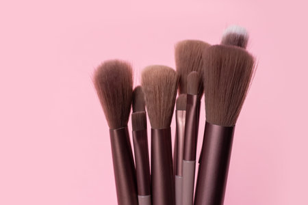 Various makeup brushes over pink background.