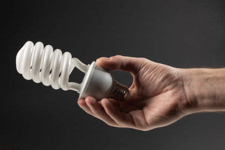 Energy saving concept. Male hand holding light bulb on dark background.