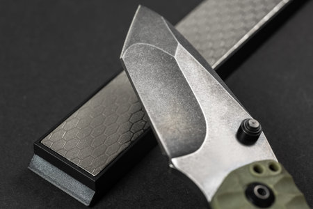 Man sharpens a knife using a whetstone on a dark table.