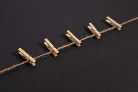 wooden clothespins on rope on dark background.