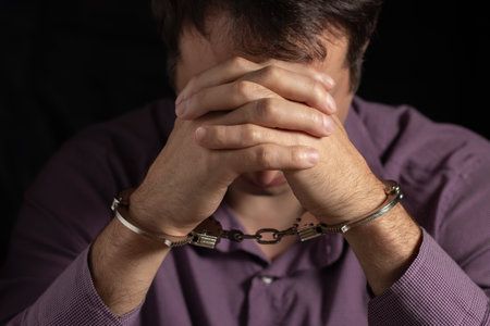Businessman in handcuffs arrested for financial fraud, sitting in interrogation room.の写真素材