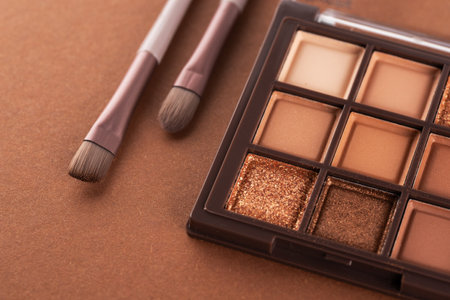 Two cosmetic brushes with light brown eye shadow dust sitting on top of palette of pale nude eye shadow shades.の写真素材