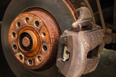 Old front brake disc with caliper and brake pads in the car, on a car lift in a workshop, close-up of a brake caliperの写真素材