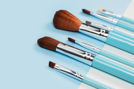 Set of makeup brushes on blue and white colored composed background. Top view point, flat lay