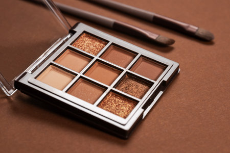 Two cosmetic brushes with light brown eye shadow dust sitting on top of palette of pale nude eye shadow shades.の写真素材