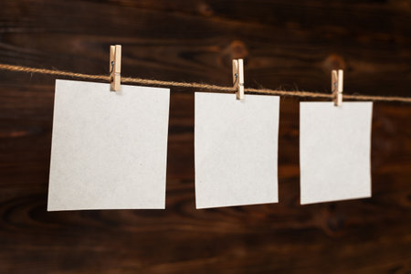 3 Note paper cards hanging with wooden clip or clothespin on rope string peg on wooden background.の写真素材