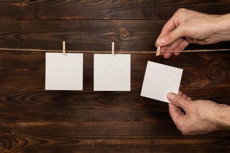 man hand take paper note cards hanging with wooden clip or clothespin on rope string peg on wooden...