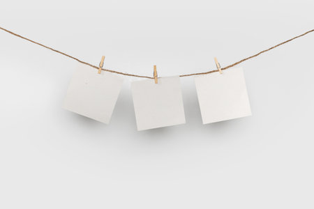 3 Note paper cards hanging with wooden clip or clothespin on rope string peg isolated on white background.の写真素材