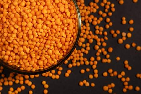 Raw red lentils are scattered out of the bowl.