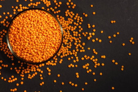 Red lentils in glass plate on dark background.