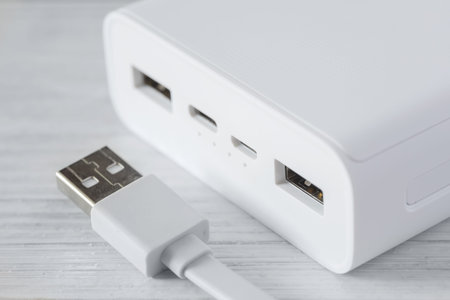 Close up of white power bank with multiple usb ports, one with plugged cable. Charging devices with...