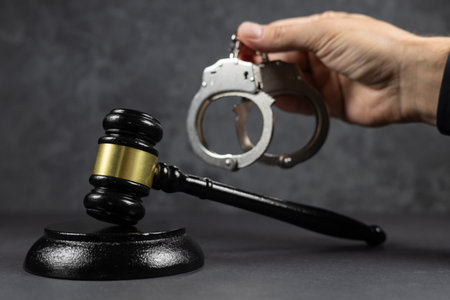 Judge's gavel and handcuffs in hand on a dark background. Judge's gavel and handcuffs.の写真素材