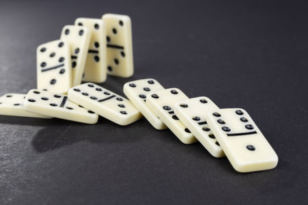 Domino effect concept with white dominoes pieces row falling on dark background. Business crisis management, finance intervention, conflict prevention or mistake consequence conceptの写真素材