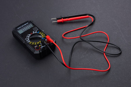 Digital multimeter with probes and display isolated on dark background. Electrical tool. Black...