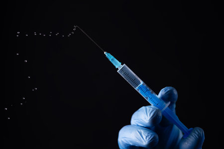 Doctors hand in surgical gloves holds a syringe on black background.