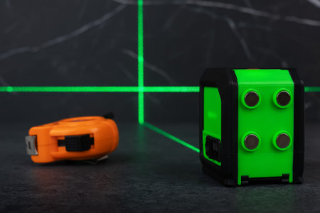Construction tools, green laser level measurer and tape measure on dark background.
