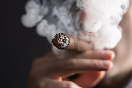 A man smokes a cigar on dark background.