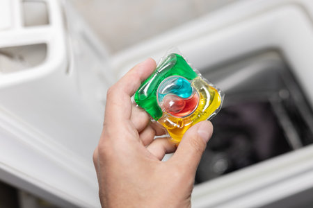 male hand holding a washing capsule against the background of a washing machine with white laundry.