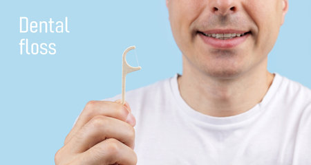 Smiling man holding a dental floss pick. Young man with dental floss pick, promoting dental hygiene....
