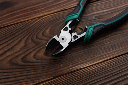 Wire cutter pliers with green handles on wooden background.