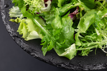 A mixture of healthy greens in a plate on a black background. Diet food.