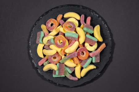 heap jelly candies on stone plate, on dark background.