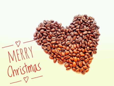 Closeup top view pile of coffee beans in heart shape with "MERRY Christmas" banner on white backgroundの素材