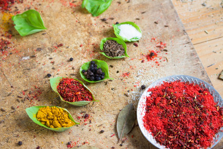 Different spices sprinkled in the green leaves on a wooden background and basil