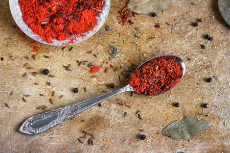 red spice mixture on the spoon and a plate on a wooden background