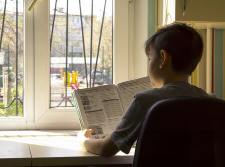 The quarantined boy sadly looks at the street through the window, there is COVID-19の写真素材
