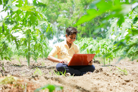 Indian boy studying in farm, holding laptop in hand , poor indian kids , day lightの写真素材
