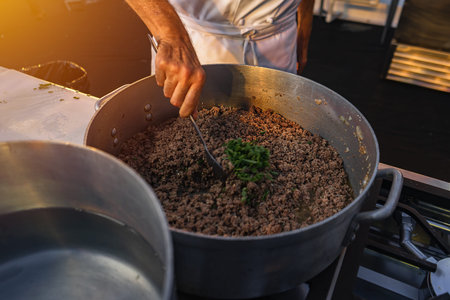 Closeup of a chefs hand stirring ground beef with oregano