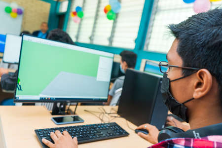 Dark-skinned Central American student in technical education glasses uses a desktop computer to do his homeworkの写真素材