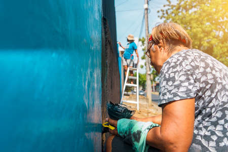 Active elderly Latin woman working outdoors painting the walls of her houseの写真素材