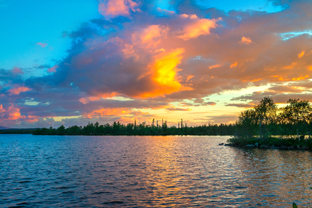 Dramatic sunset in the Arctic. The sun hiding behind the horizon, paints the clouds in a very beautiful color. Fire in the sky over the lake. On the horizon are seen the distant mountains and forestの写真素材