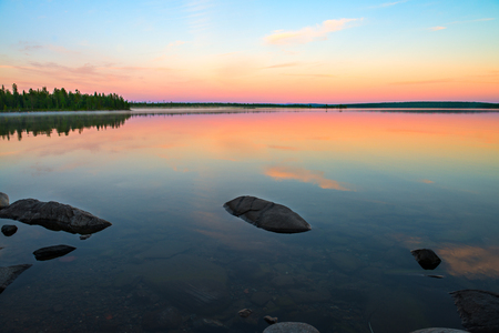 Endless polar day in the Arctic. The lake turned into a mirror. Many beautiful combinations of warm orange and cool blue. Beautiful sky reflected in the lake. In the lake a lot of round stonesの写真素材
