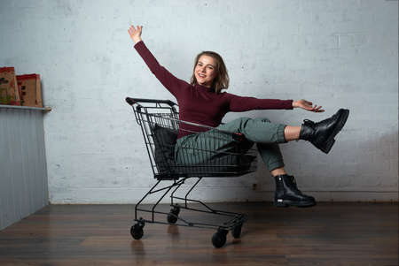 a girl in a red turtleneck sits in a shopping basketの写真素材