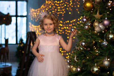 a little girl in a pink dress and a crown near the Christmas tree with gifts.の写真素材