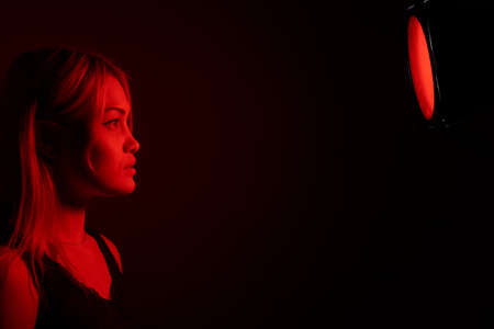 portrait of a blonde girl with bright makeup in red light.の写真素材