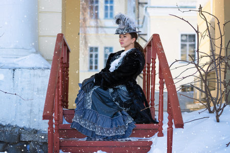a woman dressed as a 19th-century noblewoman sits on a porch near the castleの写真素材
