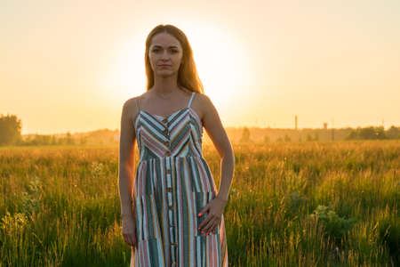 a girl in a dress in a green field in the bright rays of the setting sunの写真素材
