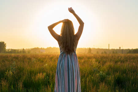 a girl in a dress in a green field in the bright rays of the setting sunの写真素材