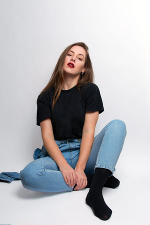 a girl with bright red lipstick, blue jeans and a black T-shirt sits on a white background.