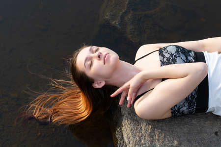 a girl in a dress on a stone in the river with a reflection of the sky with clouds in the waterの写真素材