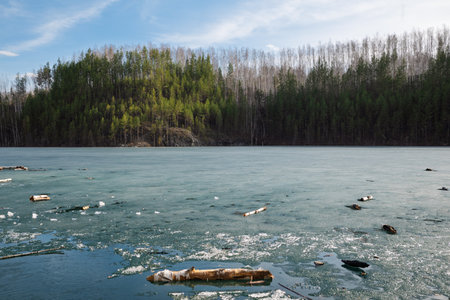 Rocky Cliff Above Frozen Lake with Pine Trees in Early Springの写真素材