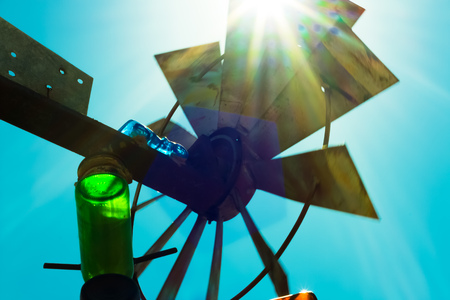 Sun shining through windmill blades while illuminating green and blue glass bottlesの写真素材