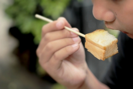 The boy eating toast topped with almonds and honey.の写真素材